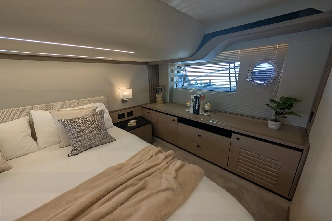 Luxurious boat cabin featuring a double bed, decorative pillows, storage units, and a window with blinds; cosy and stylish.
